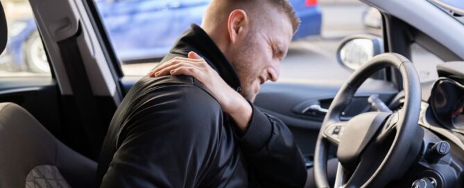 man sitting in his car after an accident holding his shoulder in pain