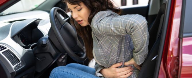 A woman sitting in her car with the door open holding the left side of her stomach in pain
